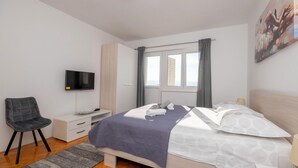 A modern bedroom with a bed, a TV, a desk, and a chair. - Apartments Ivan (Omis)