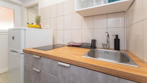 A modern kitchen with a wooden countertop, stainless steel sink, and white cabinets. - Apartments Ivan (Omis)