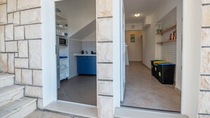 A modern kitchen with blue cabinets, a microwave, and a sink. There are trash bins and a white door leading to another room. - Apartments Ivan (Omis)