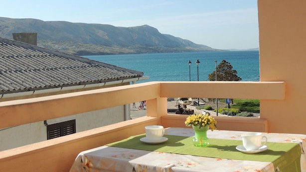A balcony with a table set for two, overlooking a coastal view with mountains in the distance. - Apartment Lina (Pag)