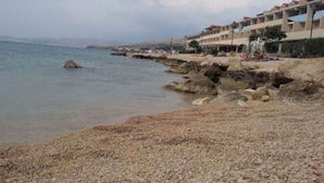 A coastal hotel with a rocky shoreline, clear skies, and a calm sea. - Apartment Lina (Pag)