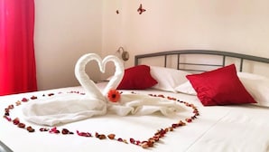 A bed with a heart-shaped towel arrangement and rose petals, red pillows, and a butterfly wall decoration. - Apartment Lina (Pag)