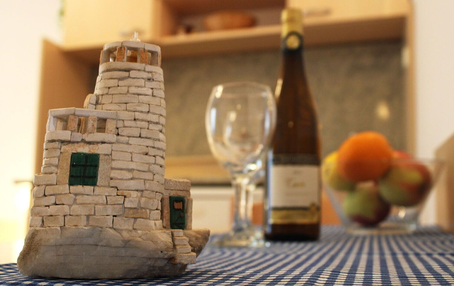 A model of a stone tower on a table, a bottle of wine, a glass, and a bowl of fruit.