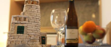 A model of a stone tower on a table, a bottle of wine, a glass, and a bowl of fruit.
