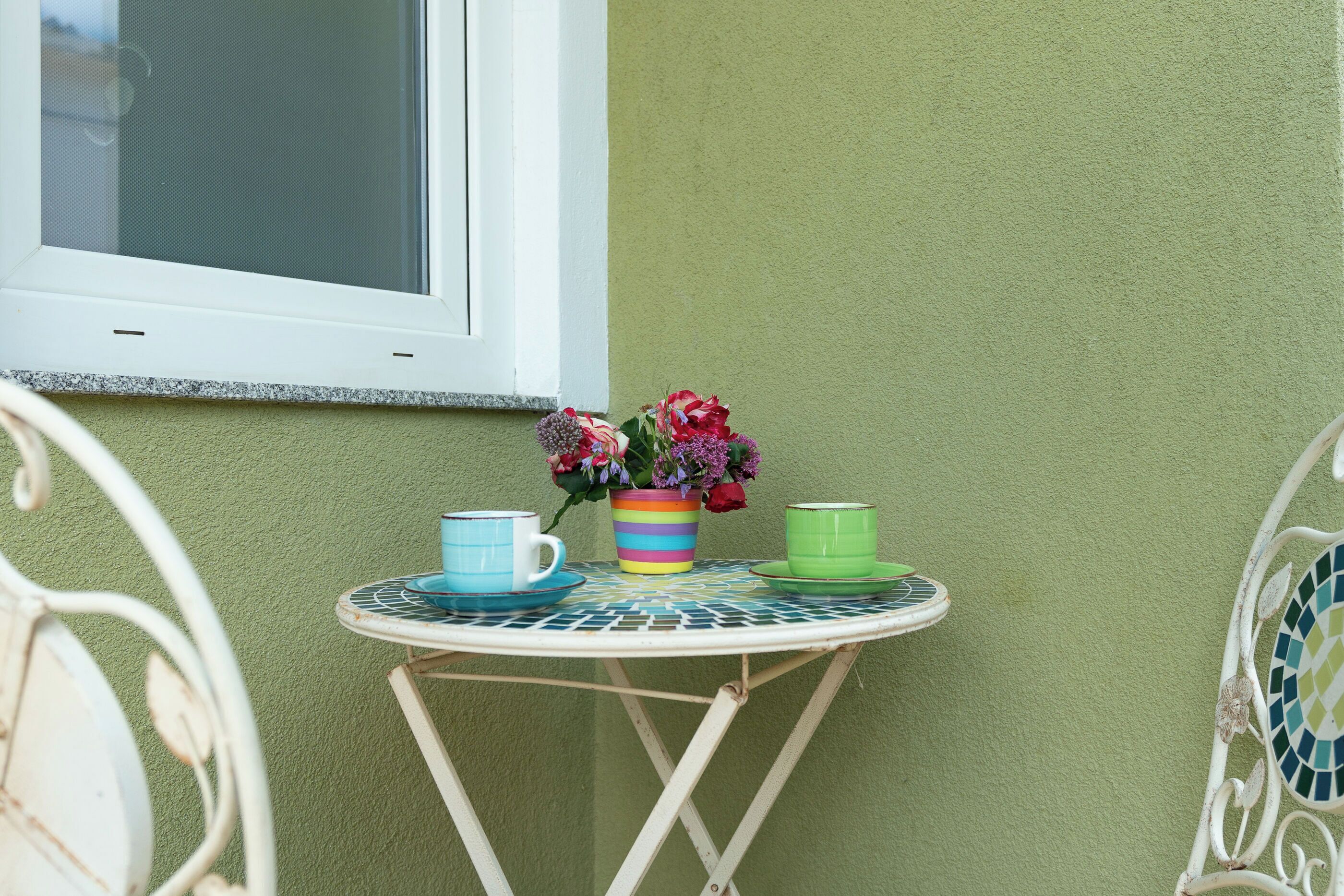 A small round table with a colorful striped mug, a green mug, and a floral arrangement.