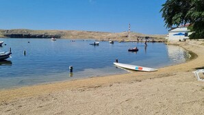 A beach with boats, a lifeguard tower, and a building with a blue umbrella. - Apartment Don (Pag)