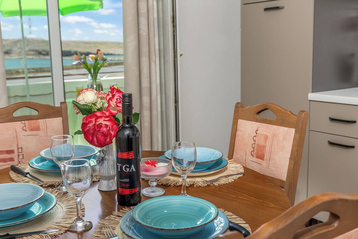 A dining table set with blue plates, wine glasses, and a bottle of red wine.