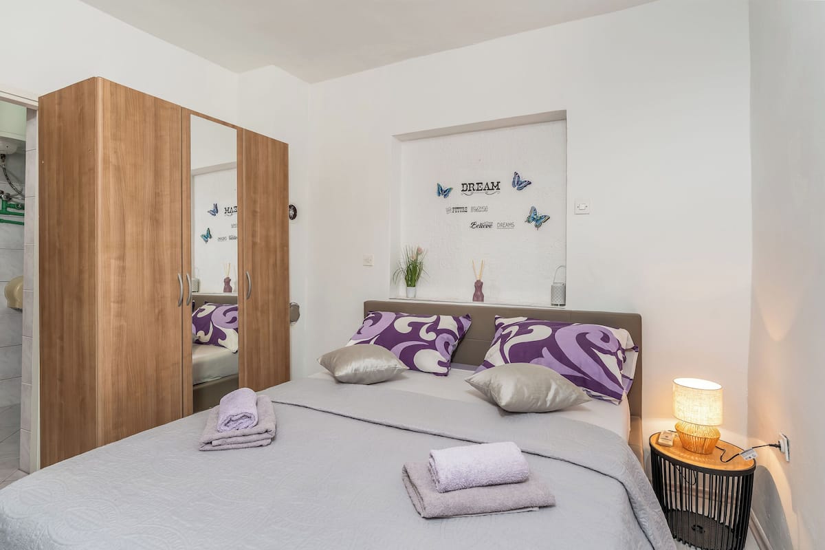 A bedroom with a bed, pillows, a nightstand, a mirror, and a wardrobe.