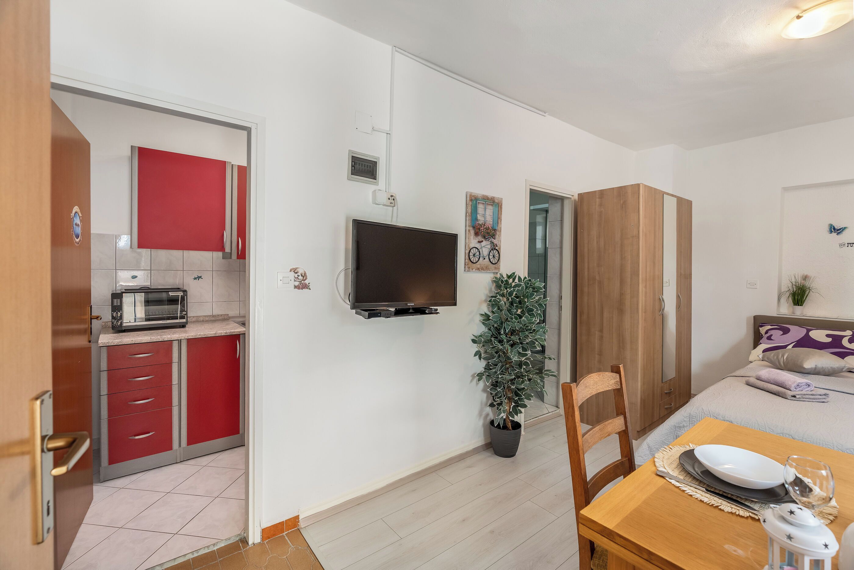 A compact room with a kitchenette, a bed, a dining table, and a television.