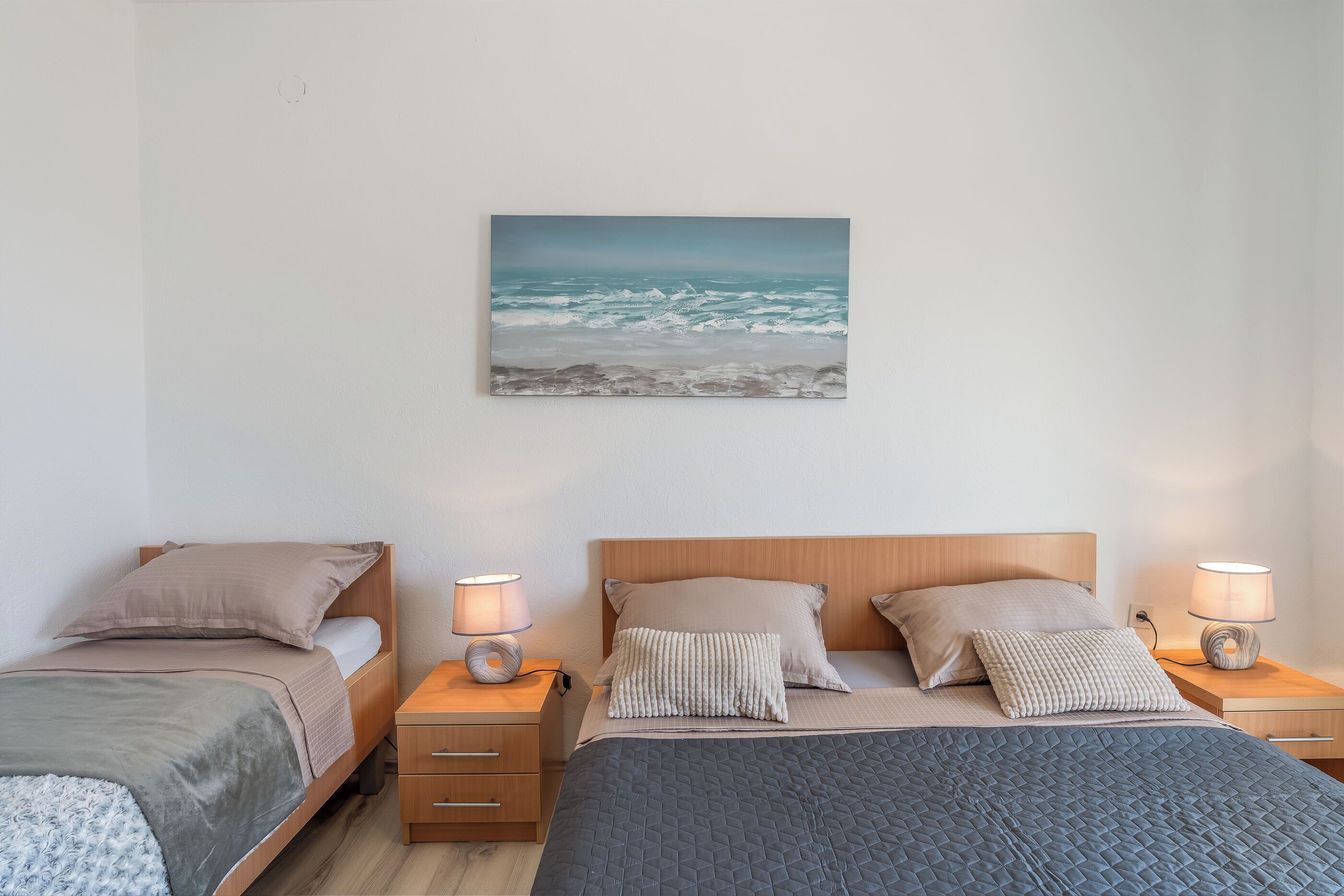Een slaapkamer met twee bedden, een schilderij van de oceaan en bedlampjes.