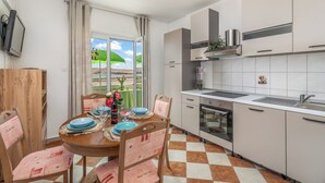 A modern kitchen with white cabinets, a built-in oven, and a large window with a view of greenery. - Apartment Don (Pag)