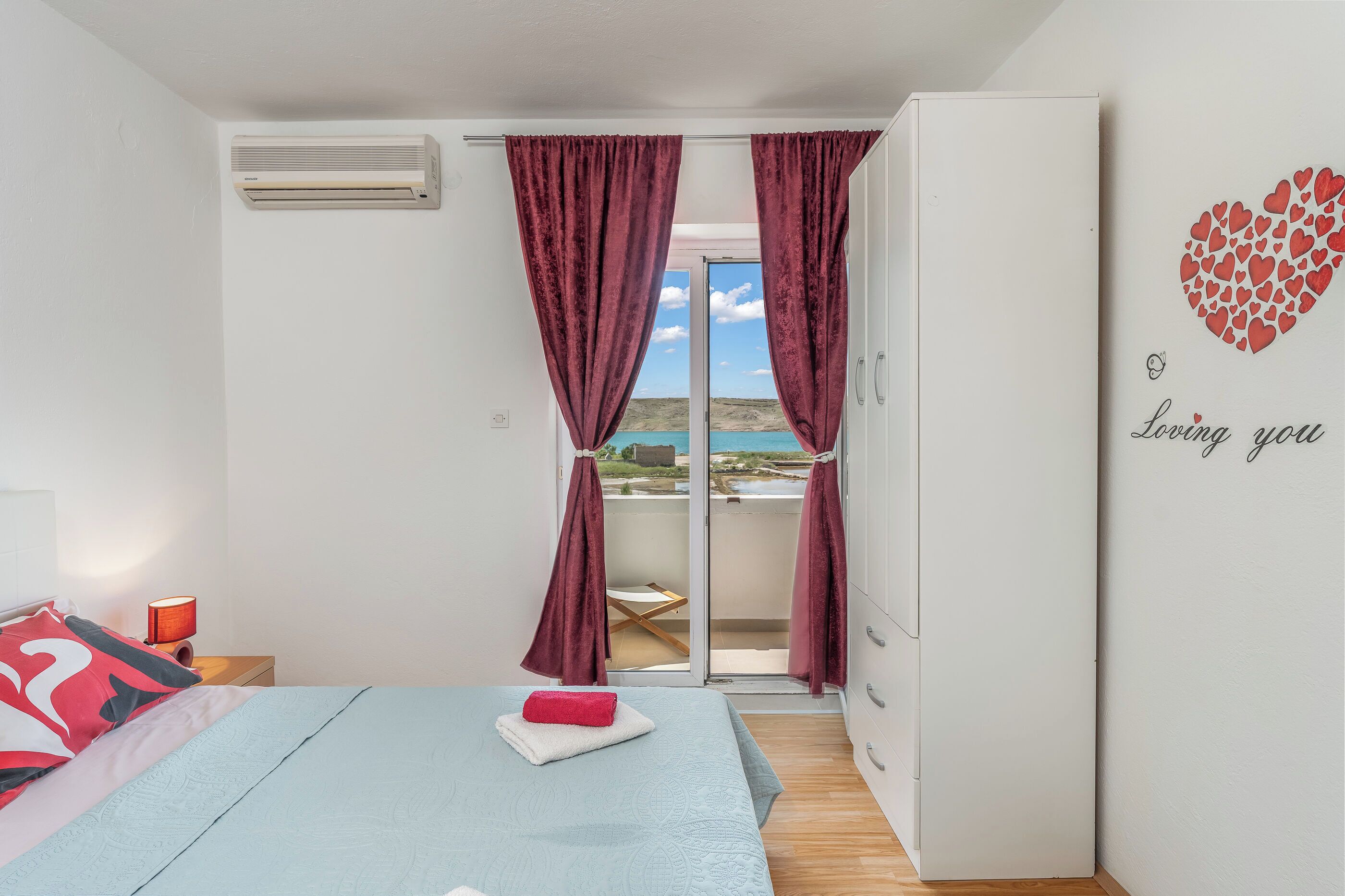 Un dormitorio con cama, mesita de noche, armario y puerta corrediza de vidrio que da a un balcón con vistas.