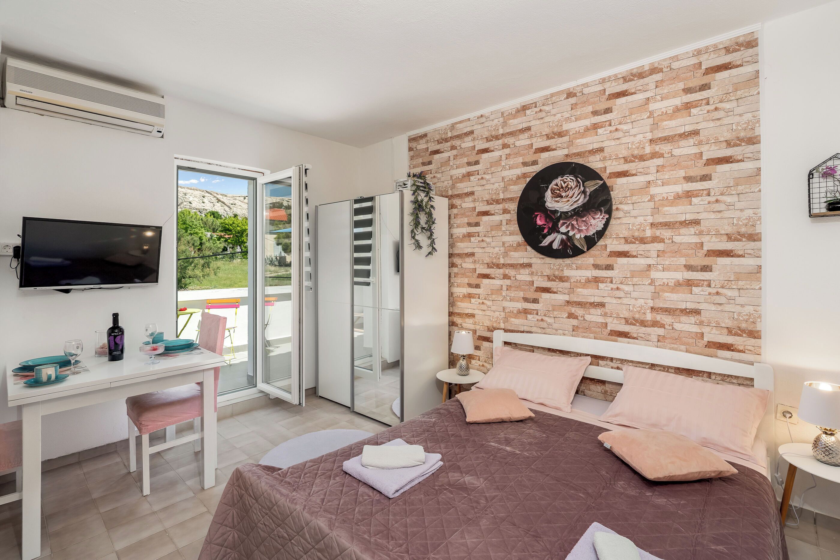 Quarto de hotel com cama, escrivaninha, televisão e varanda com porta de correr.