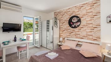 Quarto de hotel com cama, escrivaninha, televisão e varanda com porta de correr.