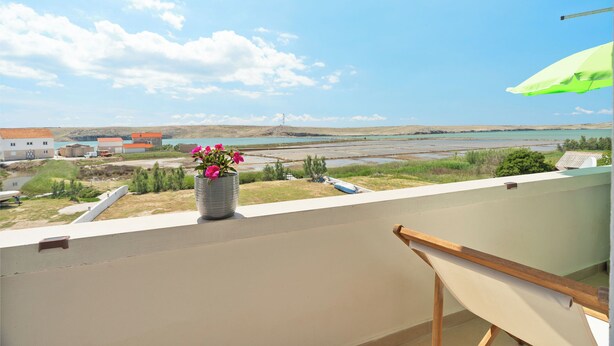A balcony with a view of a coastal landscape, a potted plant, and a green umbrella. - Apartment Don (Pag)