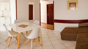A living room with a brown sofa, a white dining table with four chairs, and a kitchen area in the background. - Apartments Marija (Murter-Kornati)