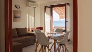 A room with a sofa, a dining table with chairs, a view of the sea through an open door, and a wall-mounted air conditioner. - Apartments Marija (Murter-Kornati)