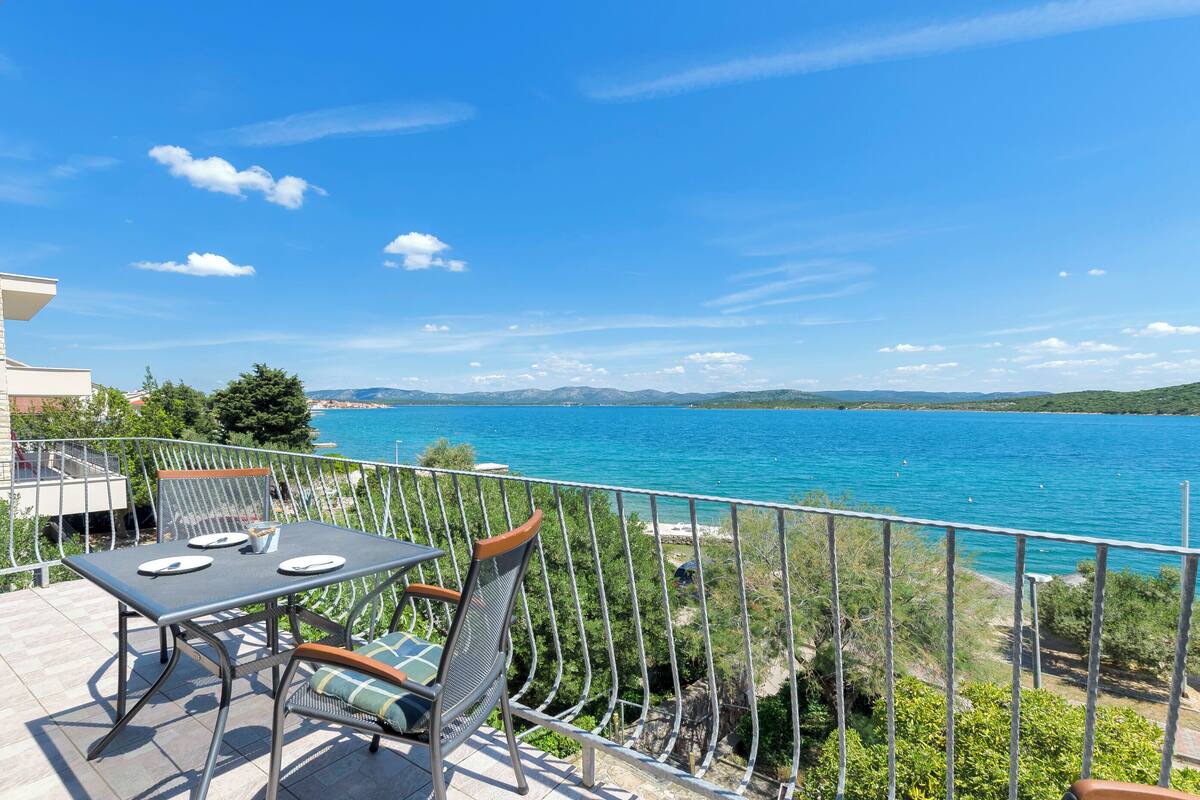 A balcony with a table and chairs overlooking a body of water and distant hills.