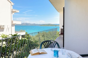 A balcony with a view of the sea, a table with a book and glasses, and a chair. - Apartments Marija (Tisno)