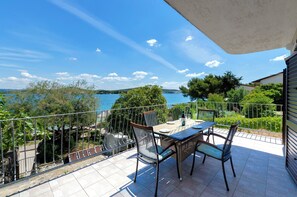 Un balcone con tavolo e sedie, affacciato su un corpo d'acqua e vegetazione.