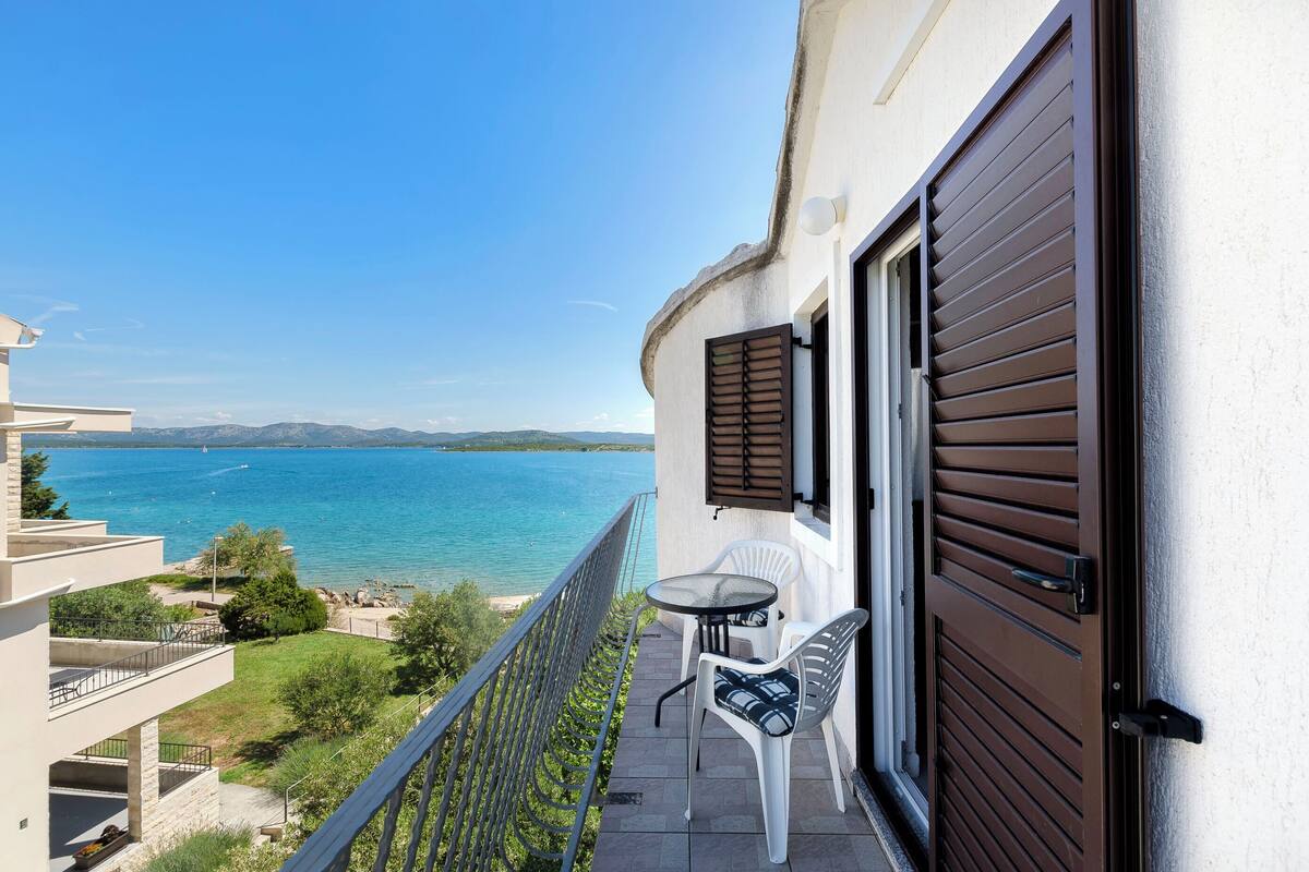A balcony with a view of the sea, a table with chairs, and a door.