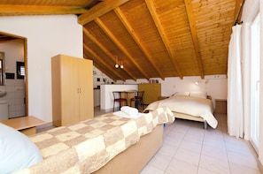 A bedroom with a wooden ceiling, a bed with a quilt, a wooden wardrobe, and a kitchenette in the background. - Apartments Marija (Tisno)