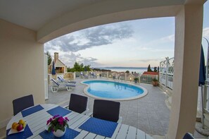 A poolside area with a view of the sea, lounge chairs, and a table with a fruit bowl and flowers. - House Jure (Selca)