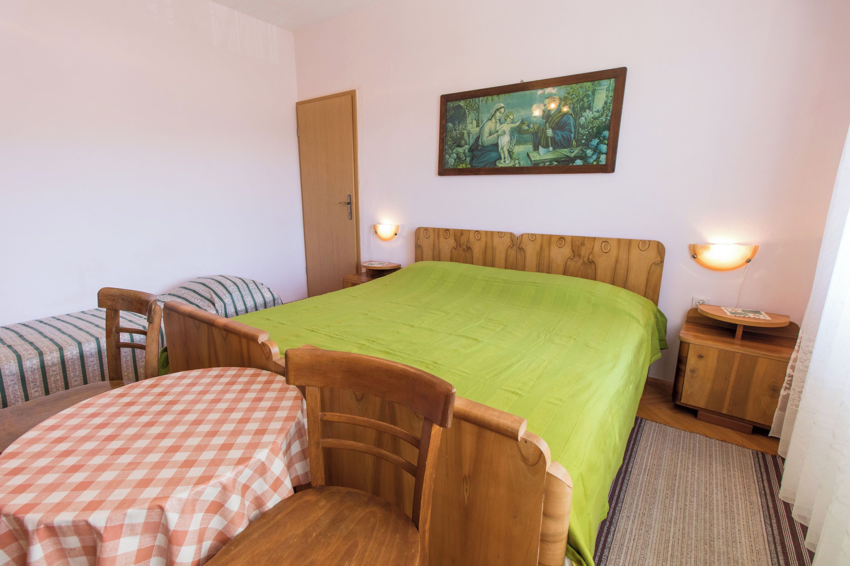 Un dormitorio con una cama grande, dos camas más pequeñas, una silla de madera, una mesita de noche y una lámpara de pared.