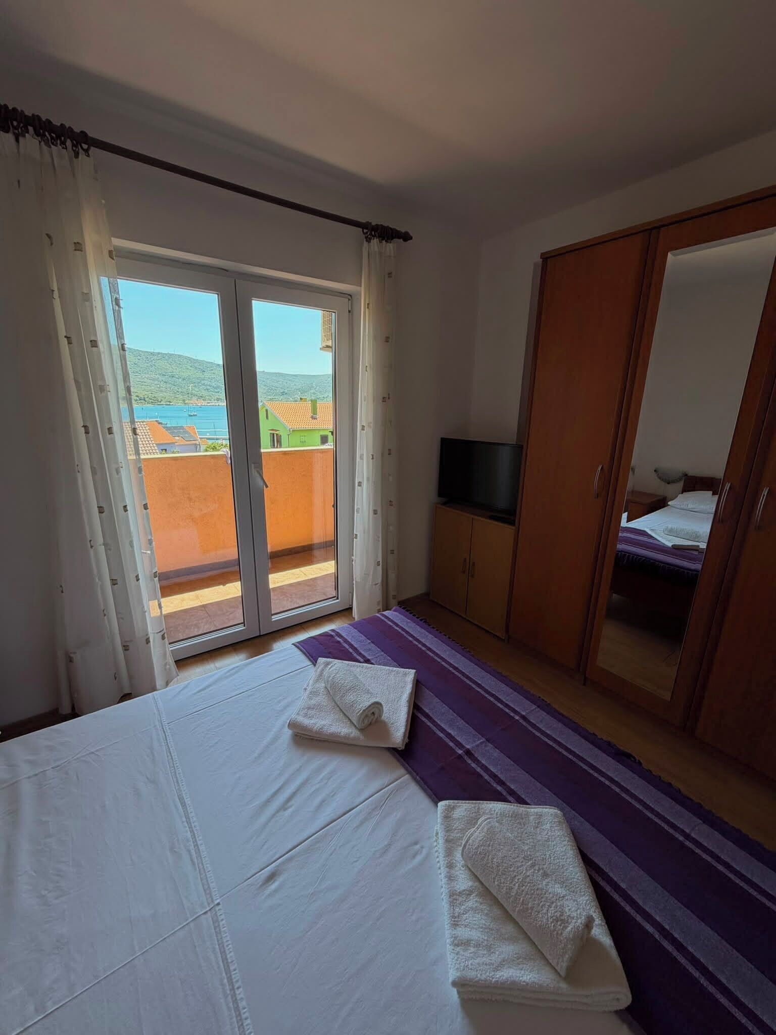 Ein Schlafzimmer mit einem Bett, einem Fernseher, einem Kleiderschrank und einer Glastür zum Außenbereich.