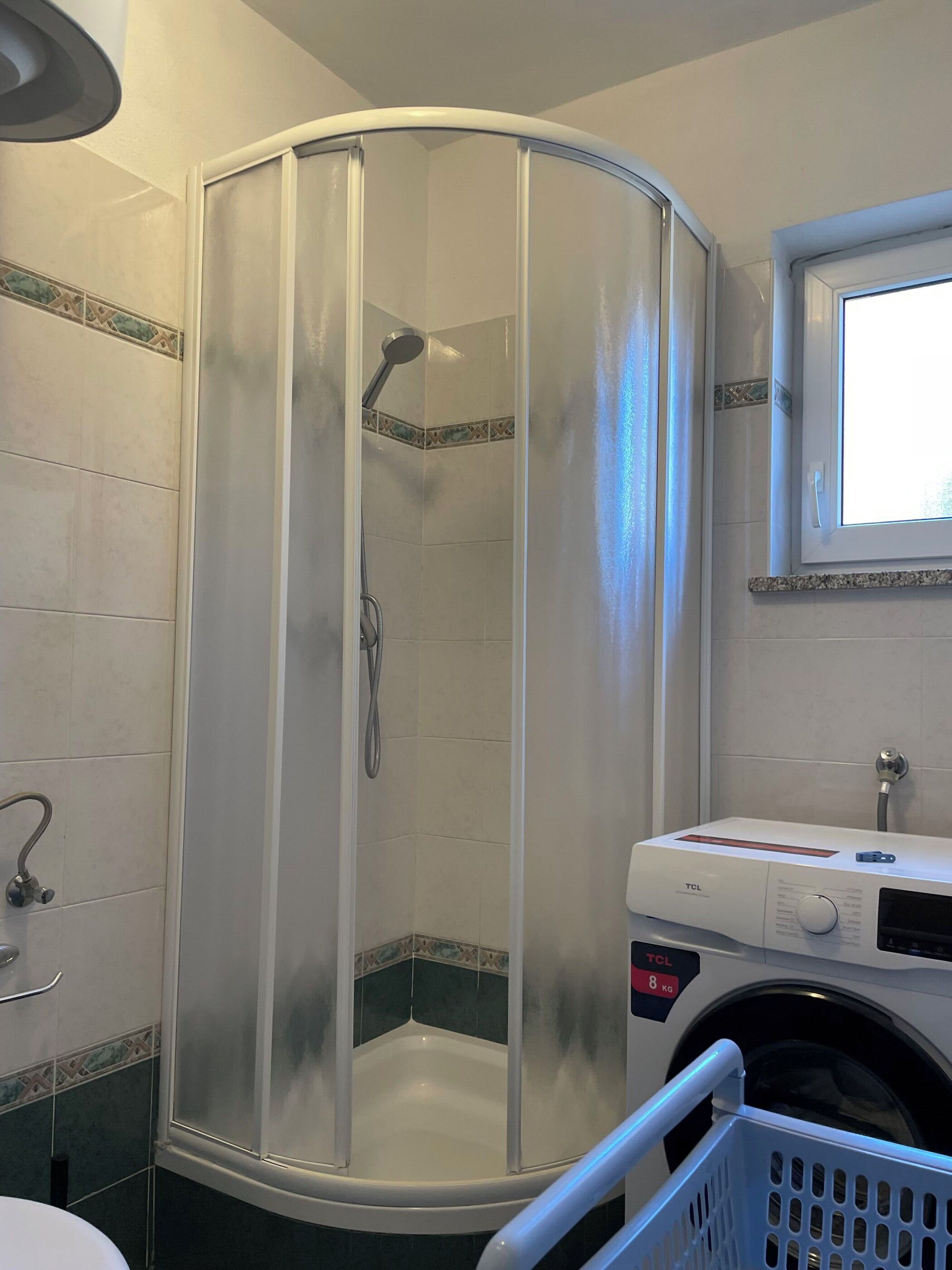 A bathroom with a shower enclosure, a washing machine, and a window.