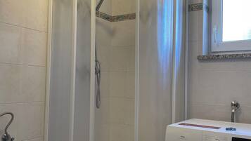 A bathroom with a shower enclosure, a washing machine, and a window.