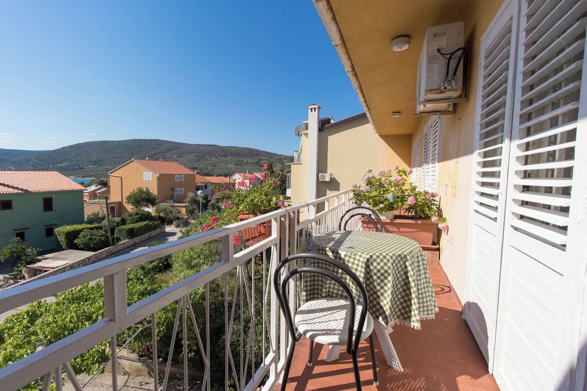 A balcony with a table and chairs, overlooking a village and hills.