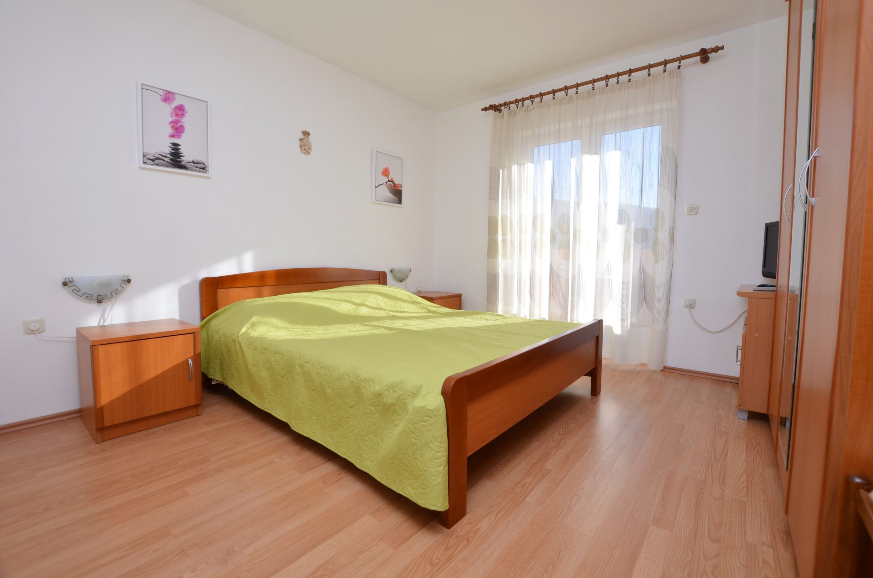 Un dormitorio con una cama de madera, una mesita de noche, un armario y una ventana con cortinas.