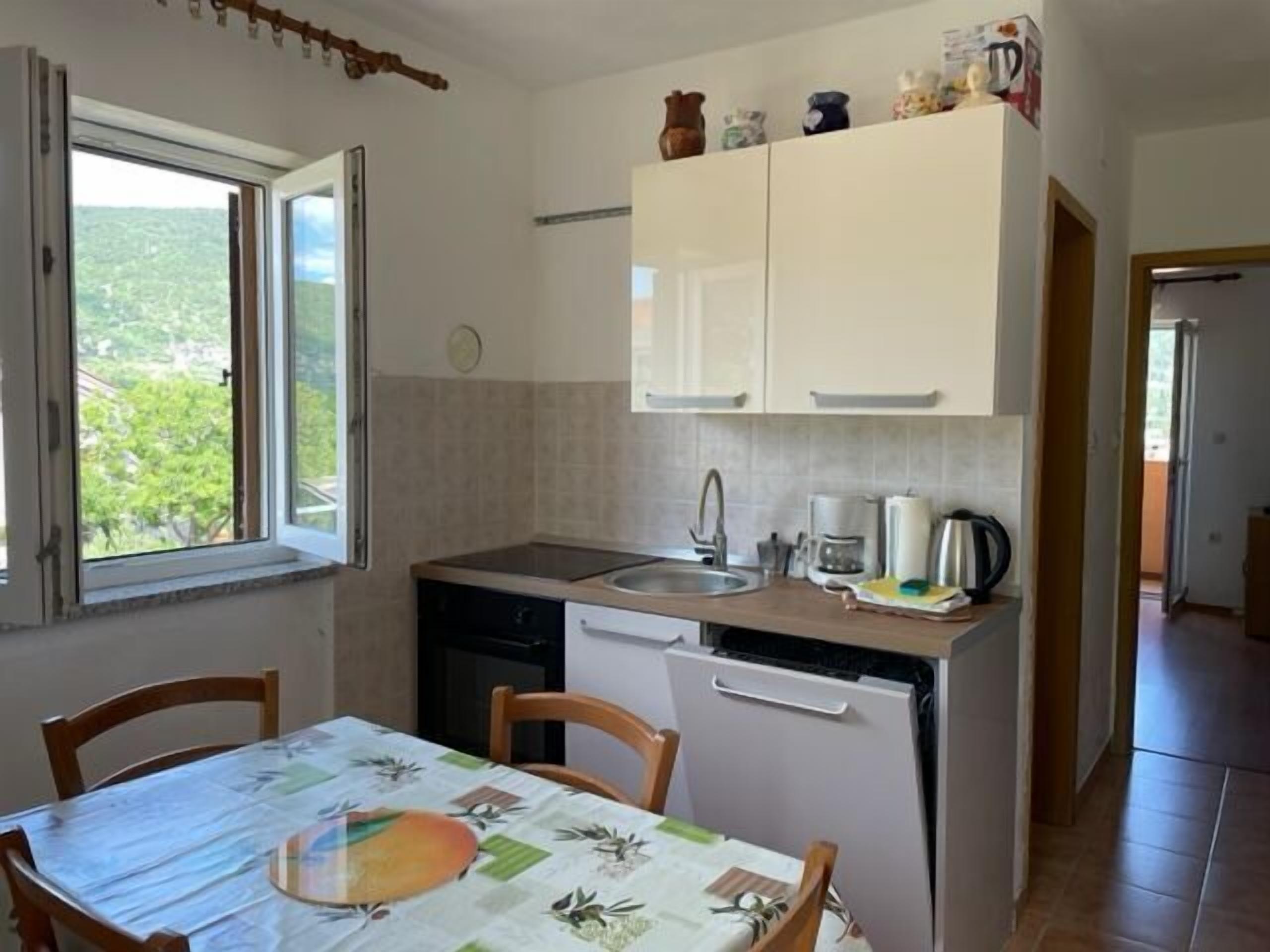 Een kleine keuken met raam, wastafel, koffiezetapparaat en koelkast.