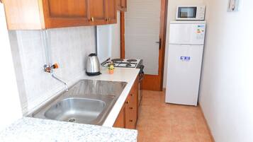 Una cocina pequeña con armarios de madera, un lavamanos de acero inoxidable, un microondas y un refrigerador.