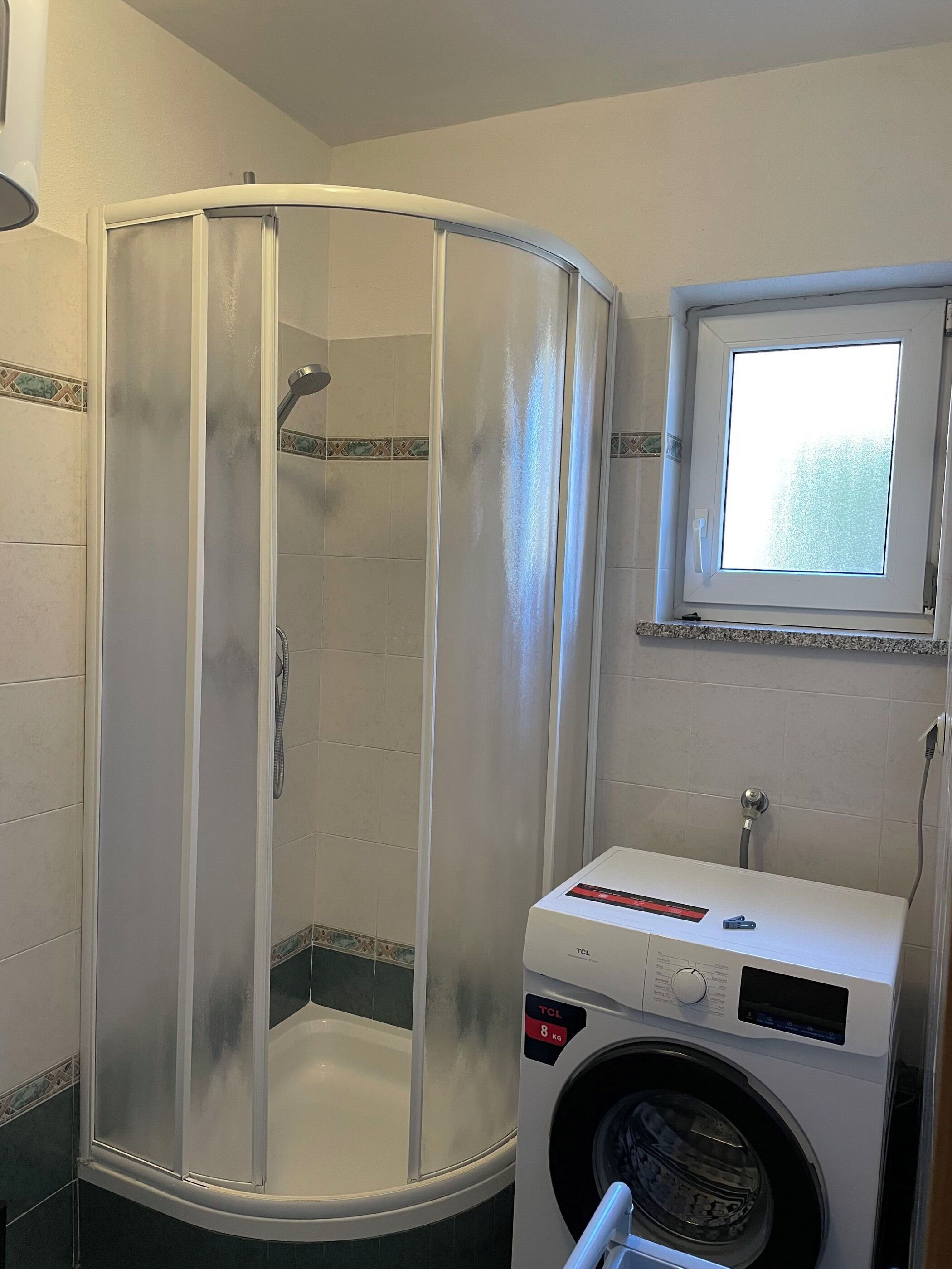 A bathroom with a shower enclosure, a washing machine, and a window.