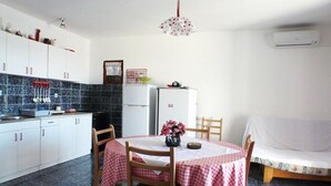 A compact kitchen with white cabinets, a refrigerator, and a dining table set with a checkered tablecloth. - Apartments Mari (Blato)
