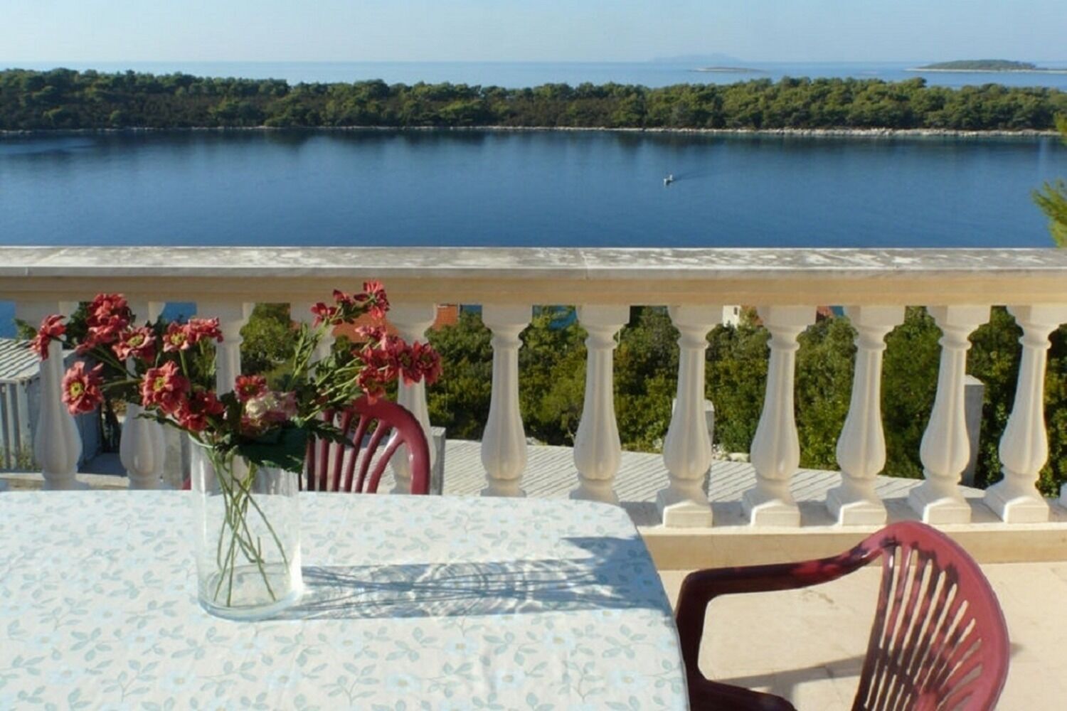 Uma varanda com mesa e cadeiras, dando vista para um lago tranquilo com uma ilha ao longe.