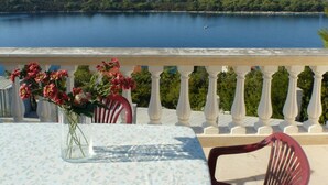 A balcony with a table and chairs, overlooking a calm body of water and a forested coastline. - Apartments Mari (Blato)