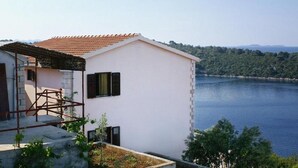 A white building with a red-tiled roof overlooking a lake, surrounded by greenery. - Apartments Mari (Blato)
