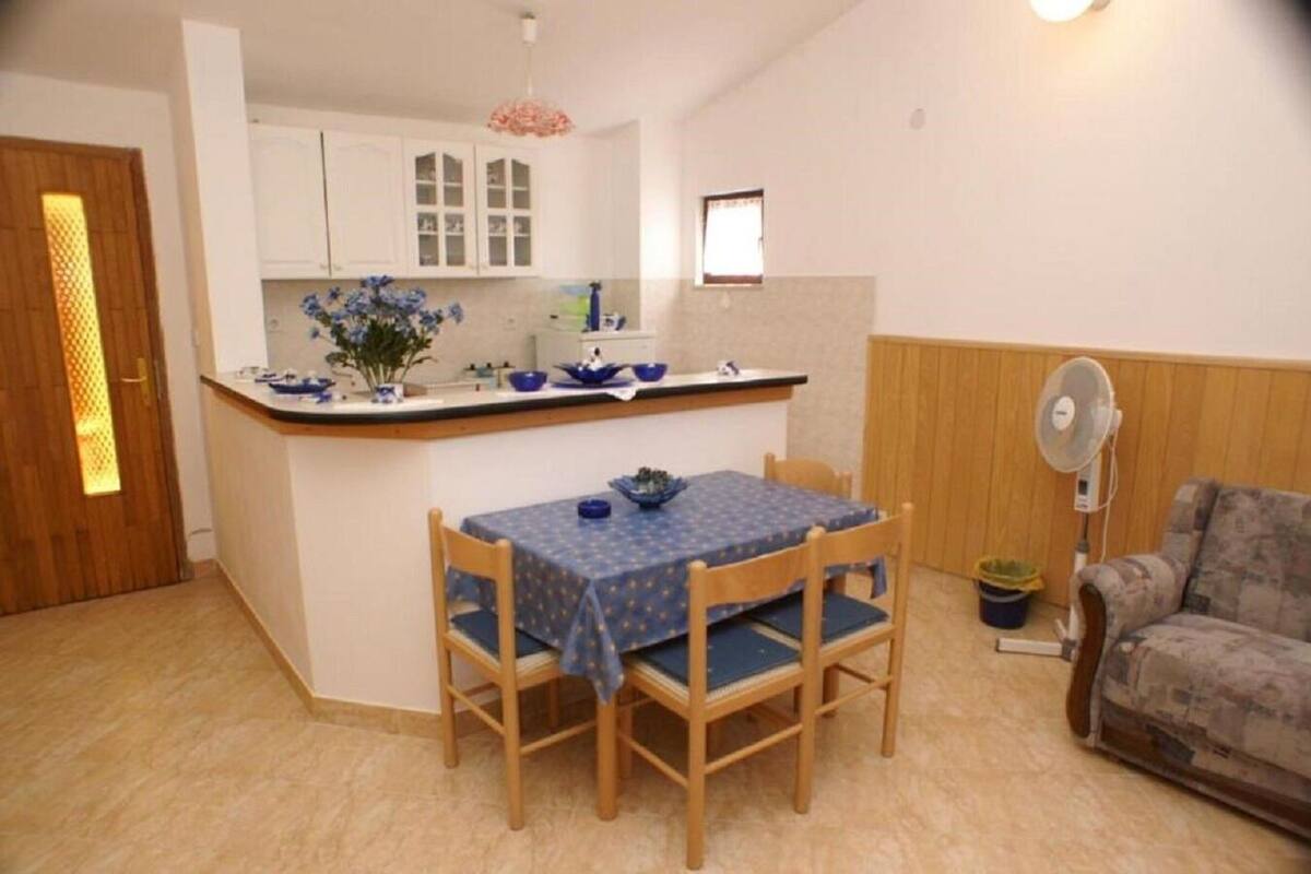 A compact living space with a kitchen area, a dining table with chairs, a sofa, and a fan.