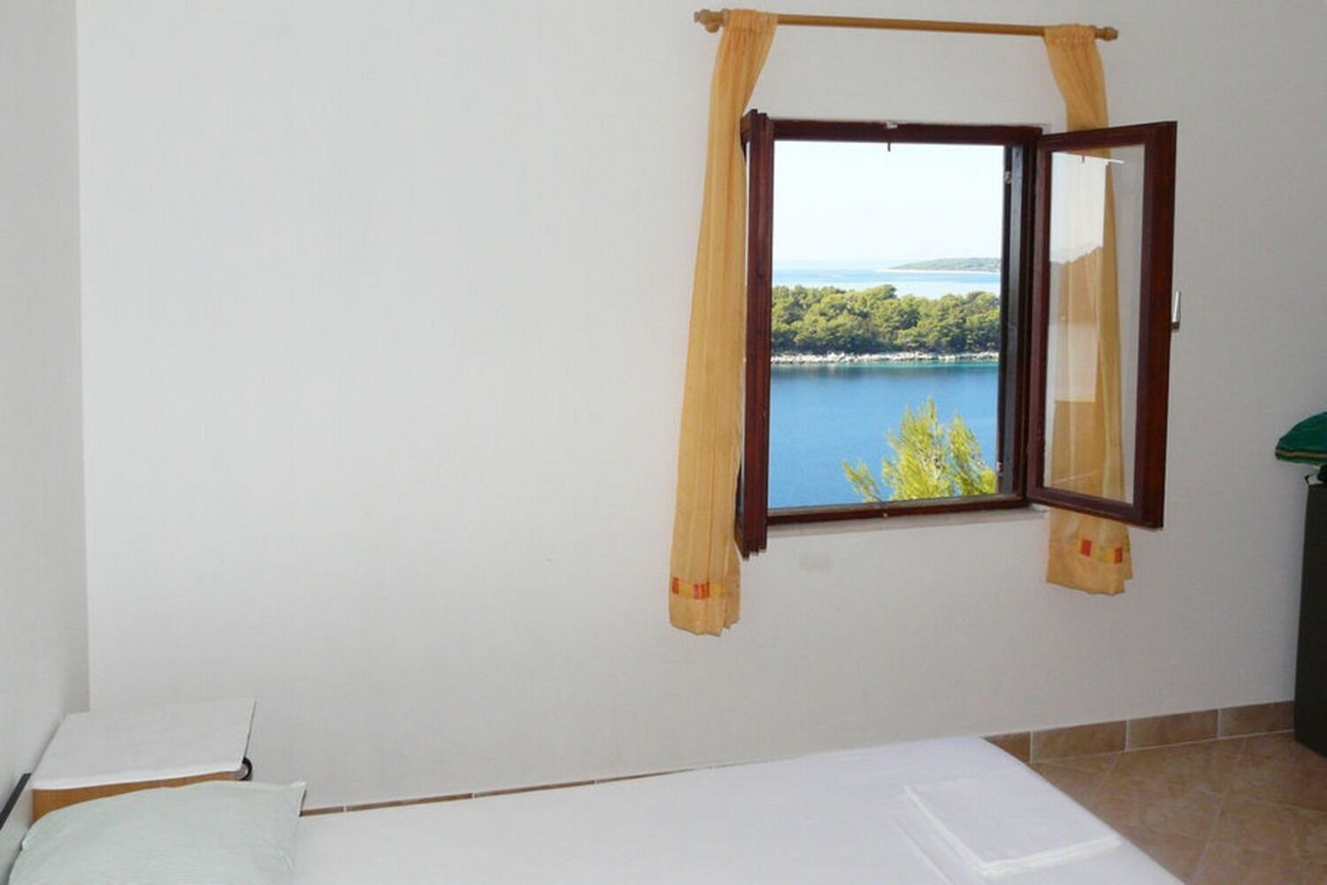 Una habitación con una cama, un ventanal con cortinas y vistas a un lago y árboles.