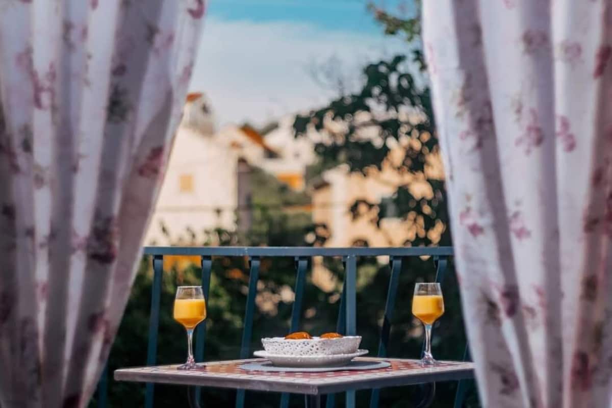 Un balcón con una mesa lista para dos personas, que incluye un plato de comida y dos vasos de jugo de naranja.
