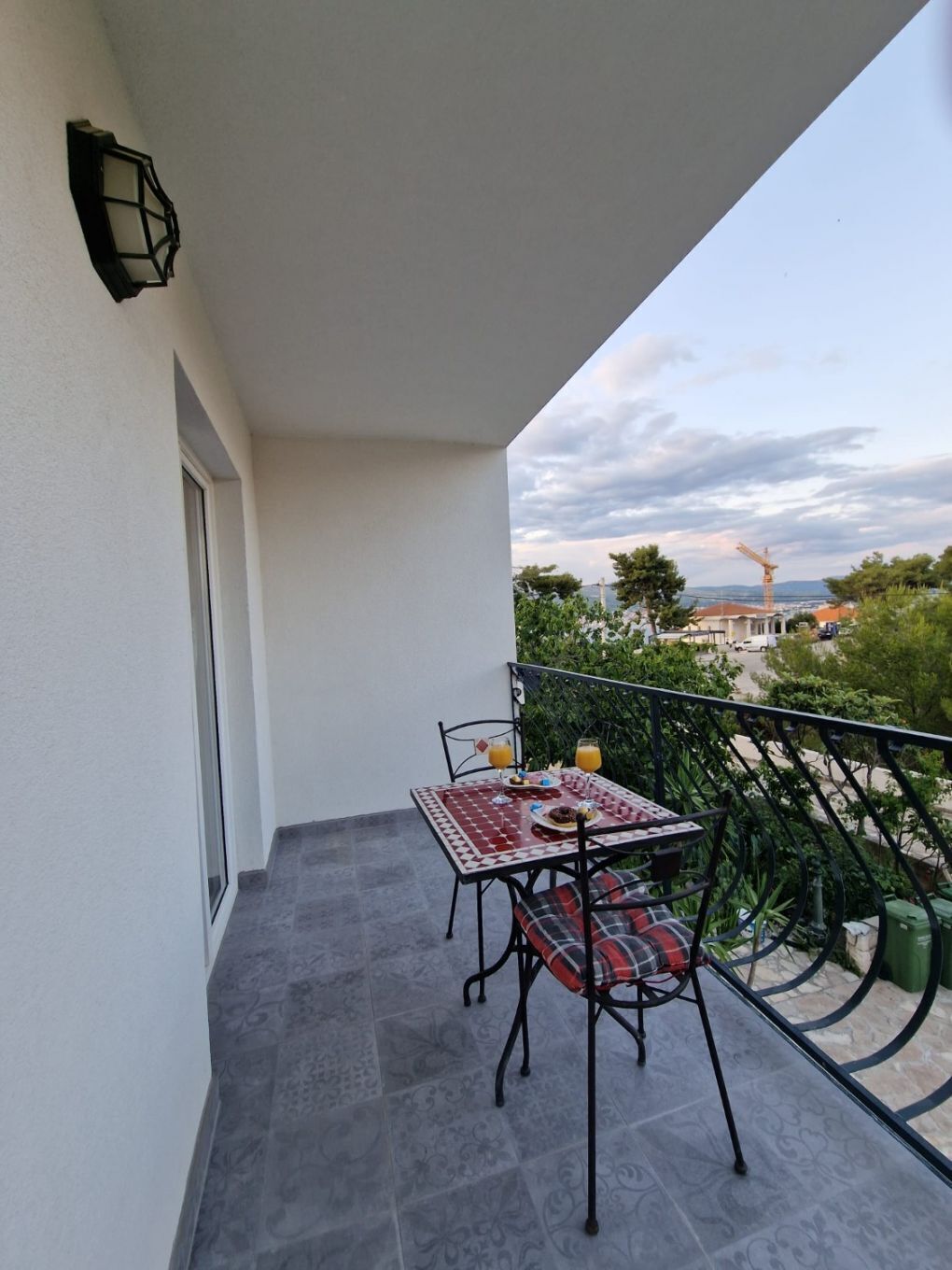 Un balcone con tavolo e sedie, vista sulla città e una gru edile in lontananza.