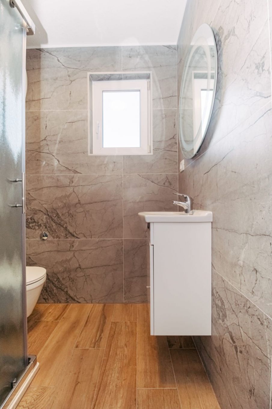 Un baño con pared de mármol, una ventana pequeña, un lavabo y un espejo.