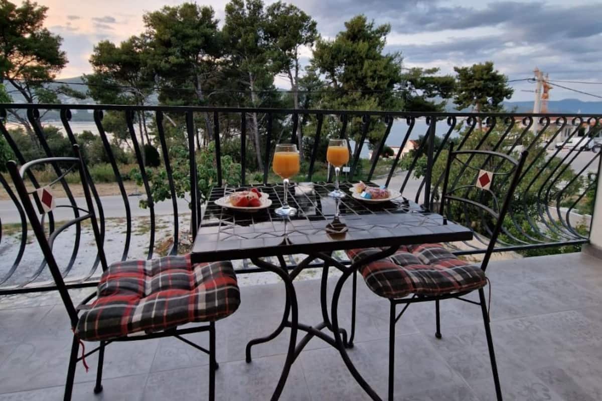 Un balcón con una mesa lista para dos personas, con cojines de cuadros y un vaso de jugo de naranja.