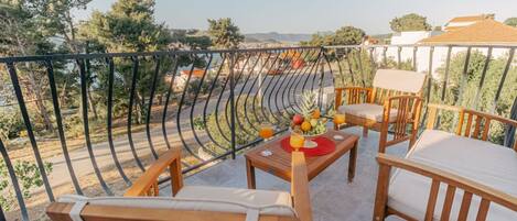 Een balkon met houten meubels, een tafel met fruit en drankjes, en uitzicht op een stadsbeeld.