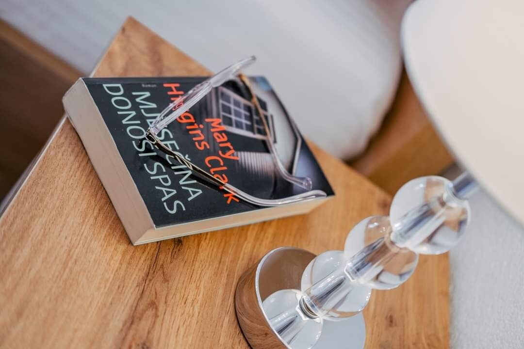 Un libro titulado “Mary Higgins Clark” sobre una superficie de madera, junto a un objeto de vidrio transparente.
