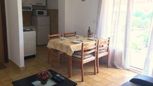 A dining area with a table set for four, a kitchen in the background, and a view through a window. - Apartments Ognjen (Tisno)