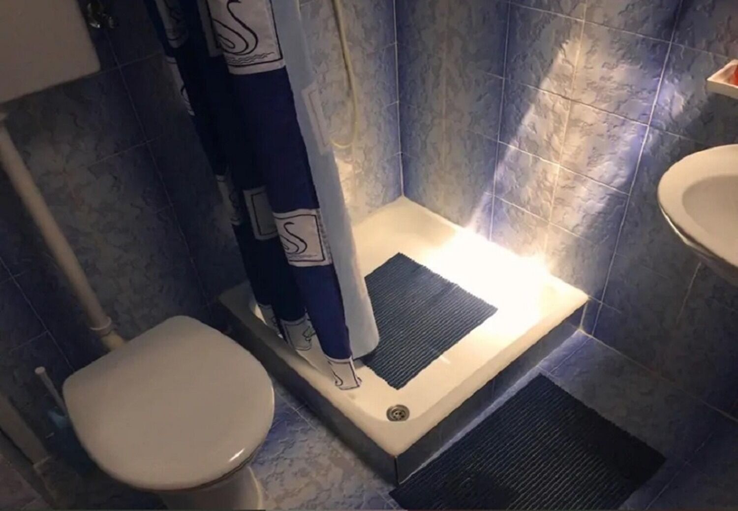 A small bathroom with a toilet, a shower with a curtain, and a sink.